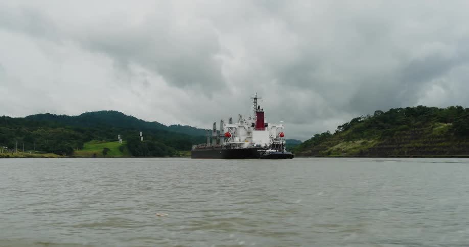 Large body of water with oil tanker in the distance and green land behind it on a cloudy day