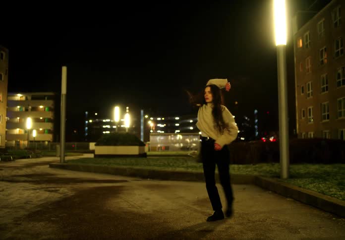 A woman is dancing in a downtown city during the night