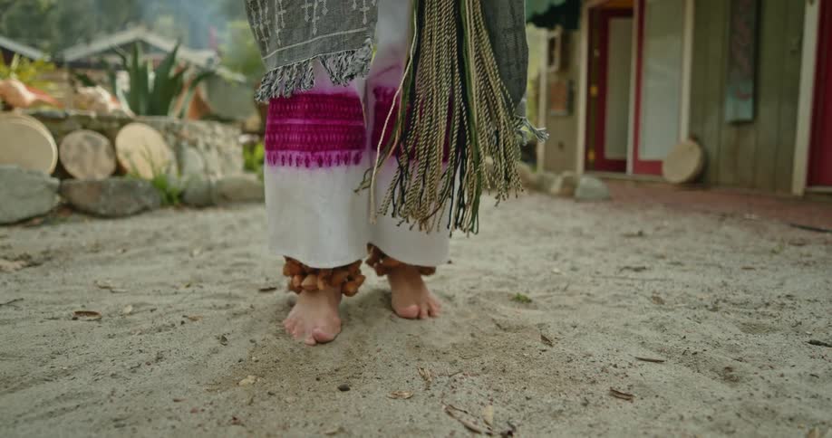 A person wearing traditional clothing dances barefoot outdoors
