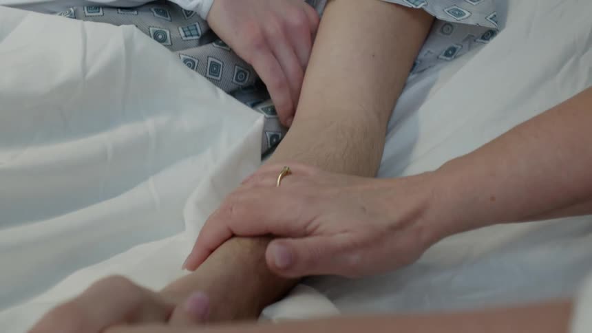 Close up of the hands of a daughter gently massaging the arm of her mother in bed