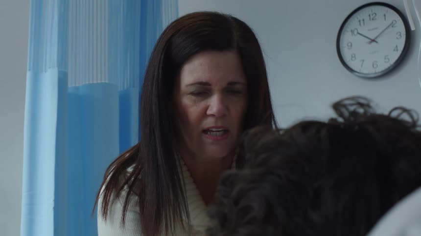 Woman touches head of patient in hospital bed and talks rapidly while looking worried