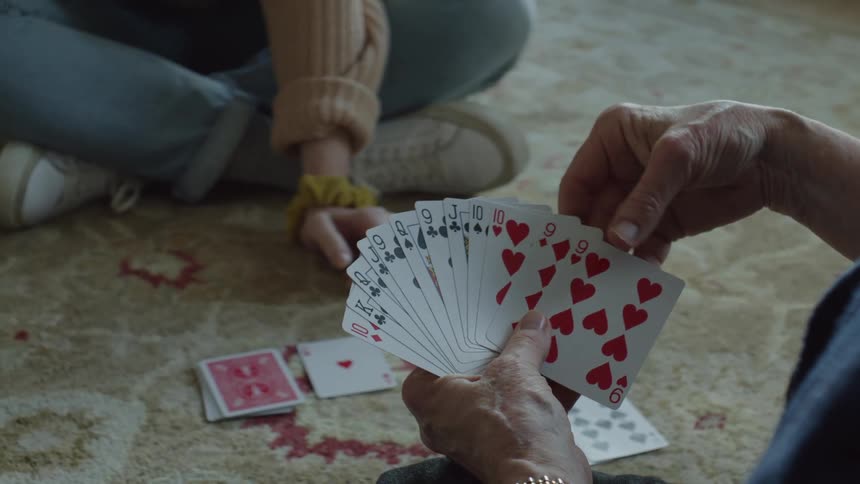 Elderly woman and young woman play spades sitting on carpet