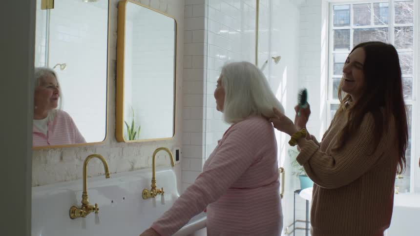 Young woman combs the long white hair of an elderly woman in the bathroom