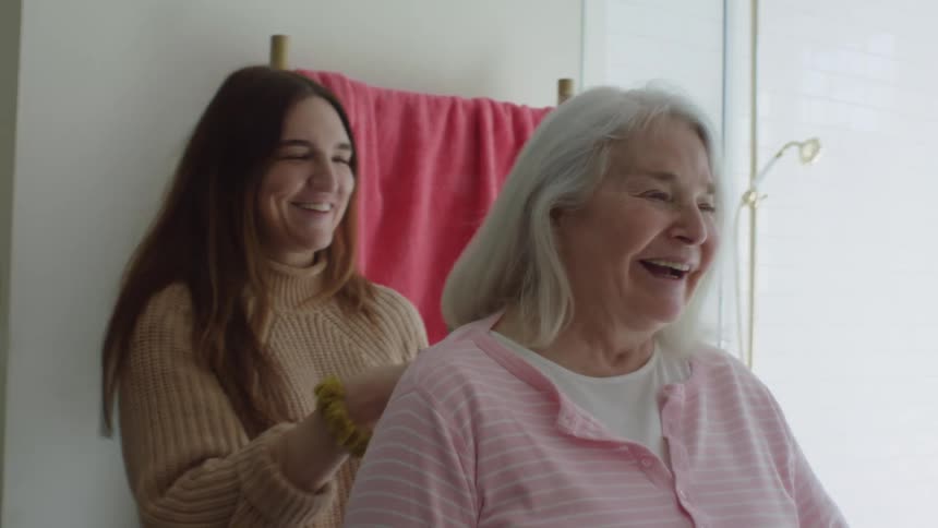 A grandaughter brushes her grandmothers hair in the bathroom while they laugh and talk