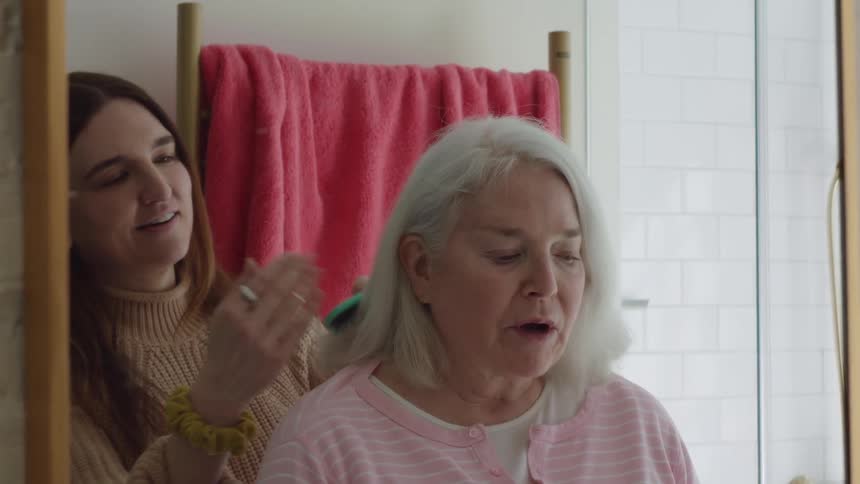 Young woman combs elderly womans hair in the bathroom