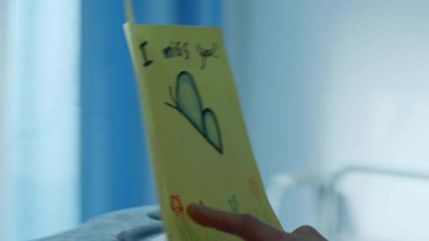 Close up of a patient reading a hand drawn card on the hospital bed