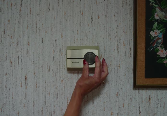 Womans hand shown turning up dial on wall thermostat