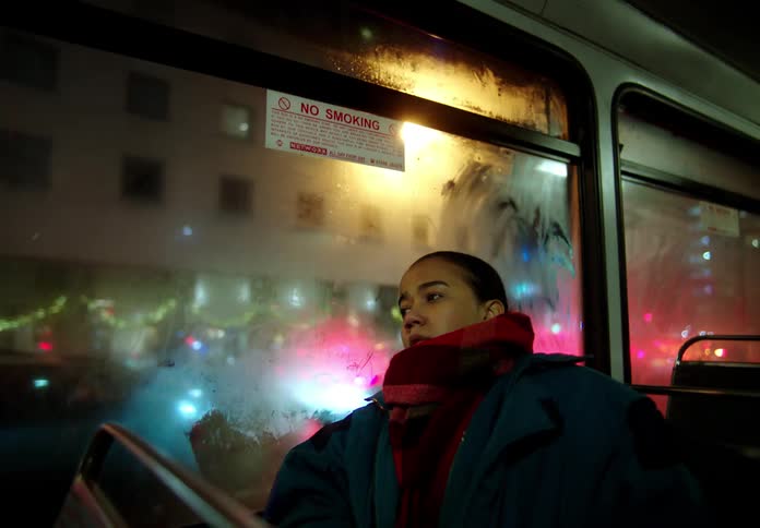 Woman with coat and red shawl travels on bus in the city at night