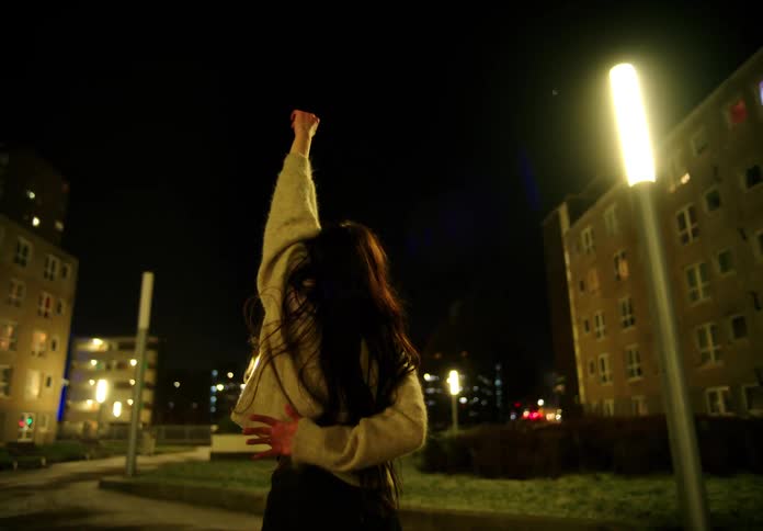 A woman moves her arms in the air as she dances on a street at night