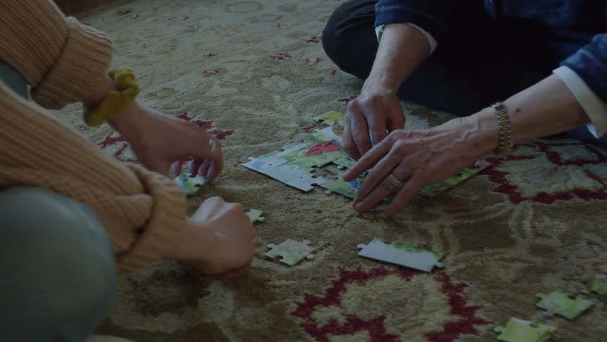 A close up of two women putting a puzzle together on a carpet sitting cross legged across from each other