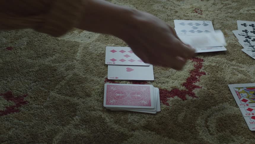 A woman is sitting on the floor playing cards on the carpet