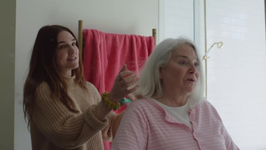 Young woman combs elderly womans hair in the bathroom