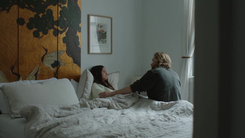 Man sitting on bed with ill woman kisses and strokes her forehead
