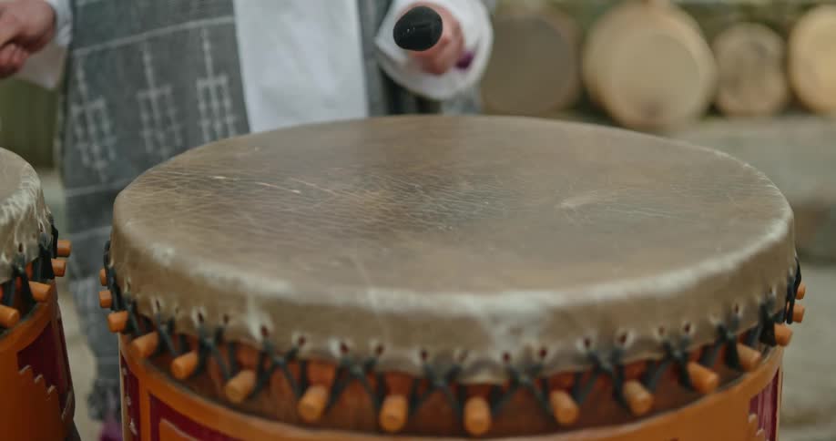 A closeup view of a set of decorated drums being hit by a person in a long robe