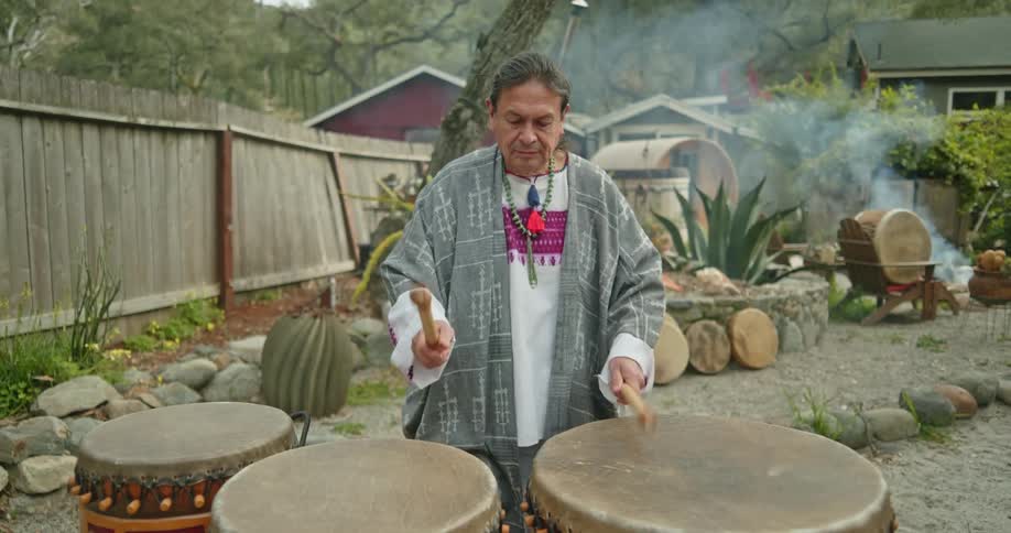 A man is playing the drums outdoors in the backyard