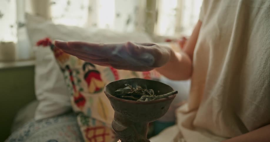 Close up of the hand of a woman gesturing over the white smoke coming out of an incense burner