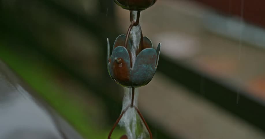 Closeup of part of hanging metal water fountain art with water running through it and dripping into water on the ground