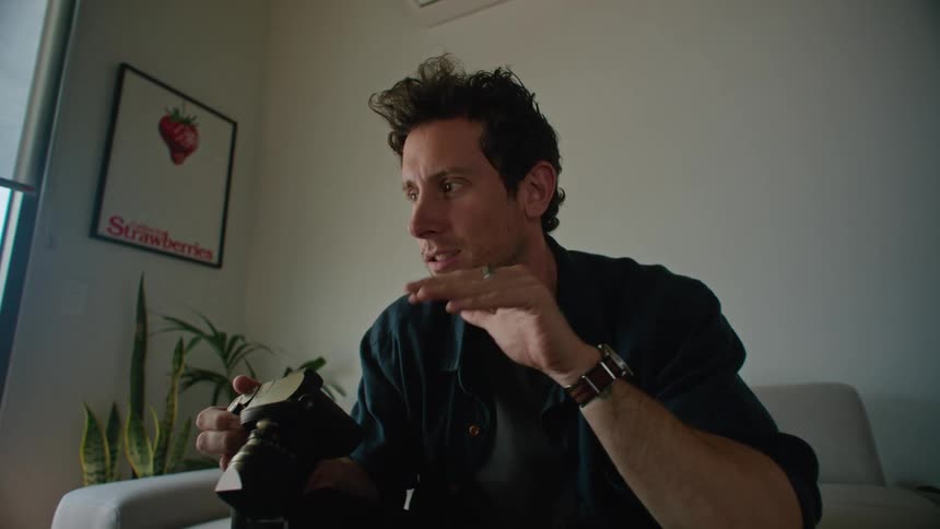 Man with black shirt watch and pants holds camera and makes video call on laptop in the living room