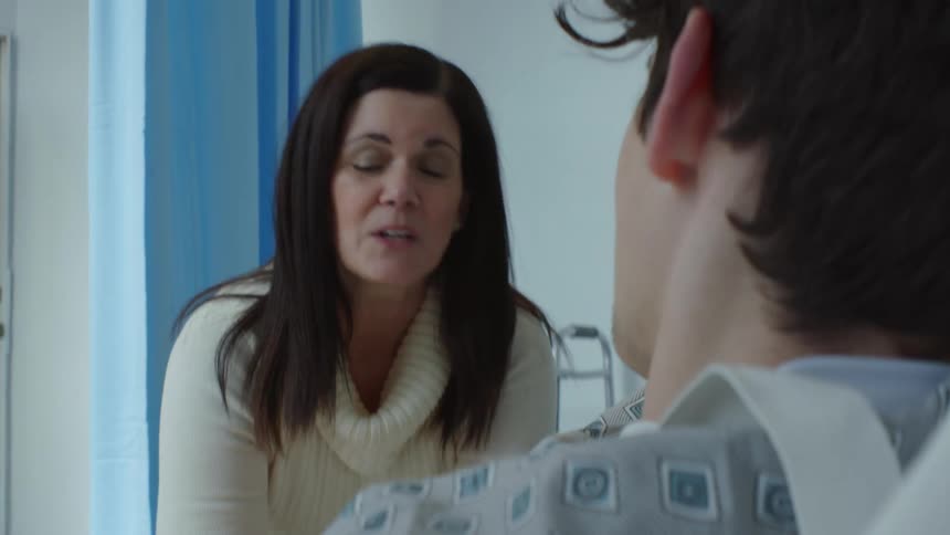 Woman talks to patient lying in hospital bed