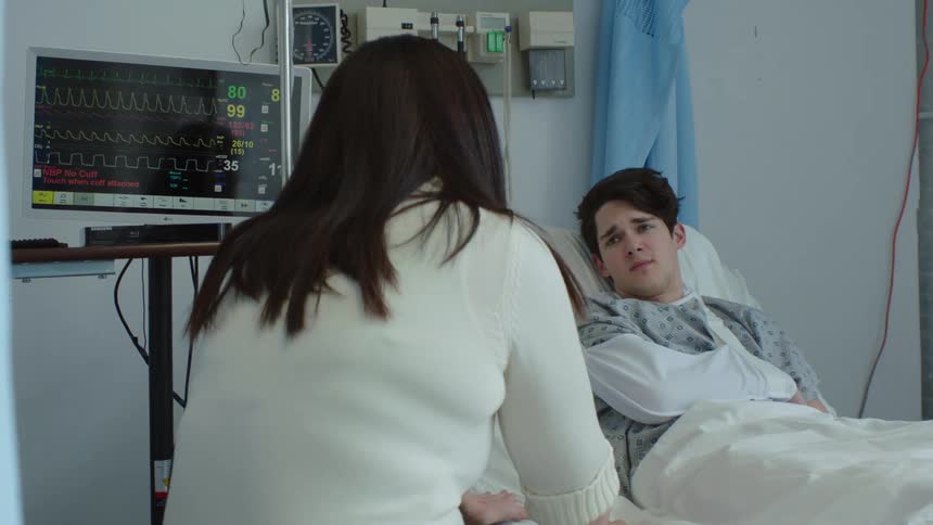 Mother talking to son who is in a hospital bed with his arm in a sling