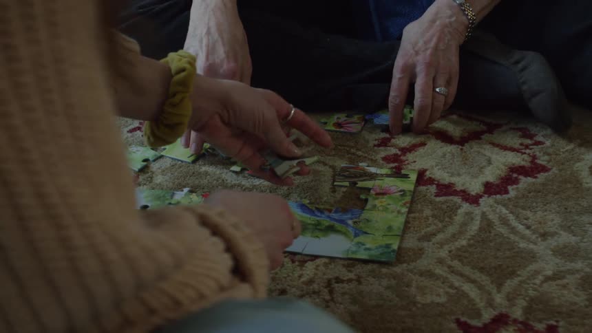 Two people put together a jigsaw puzzle while sitting on carpet