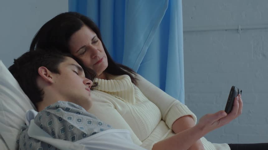 A mother watches a cell phone video with her sick son in the hospital