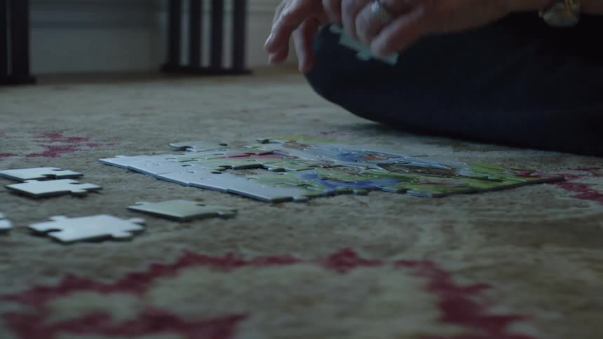 Young woman and grandmas hands doing jigsaw puzzle on the floor with carpet during the day