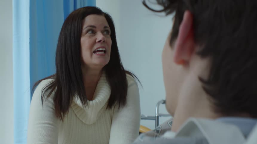 A woman is speaking to her teenage son as she visits him in the hospital