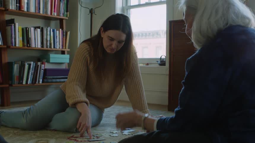 Elderly woman and young woman do puzzle sitting on carpet in the living room