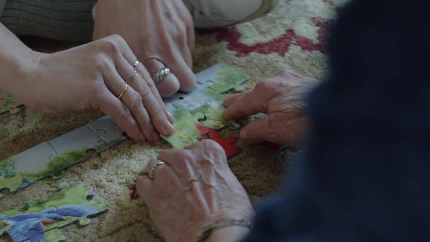 Two people are sitting indoors and completing a puzzle together