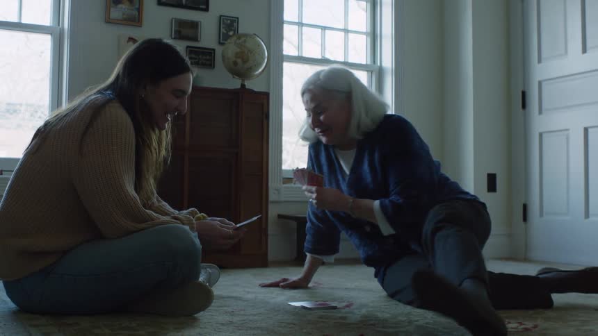 A woman laughs while playing cards with her granddaughter