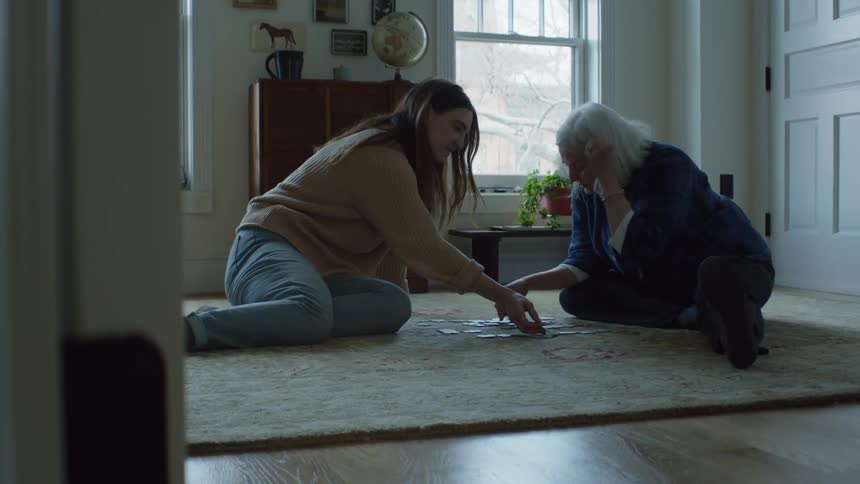 Elderly woman and young woman do puzzle sitting on carpet