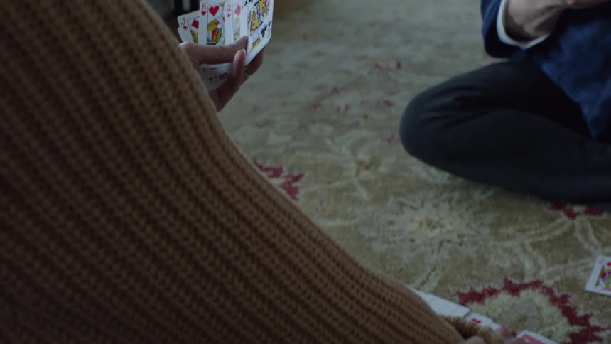 Elderly woman and young woman play spades sitting on carpet