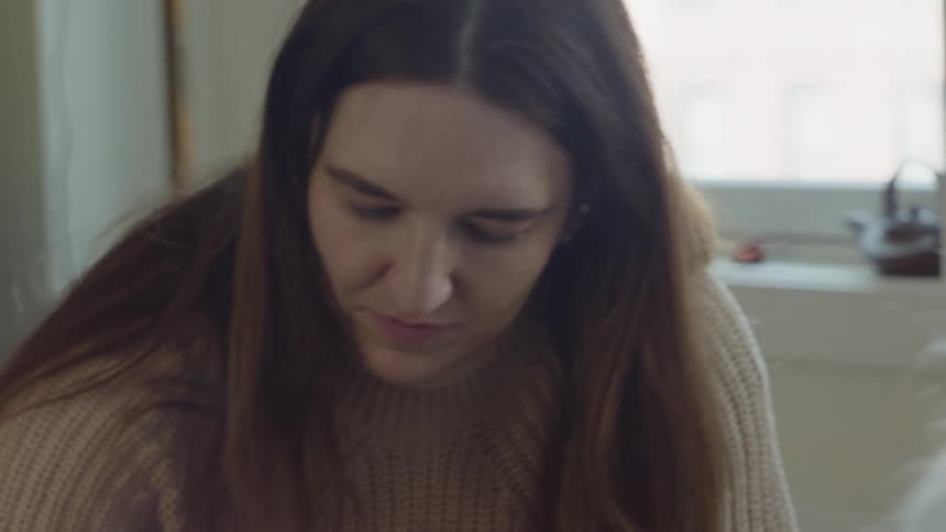 Woman focused on task talks and smiles with another person in room near window