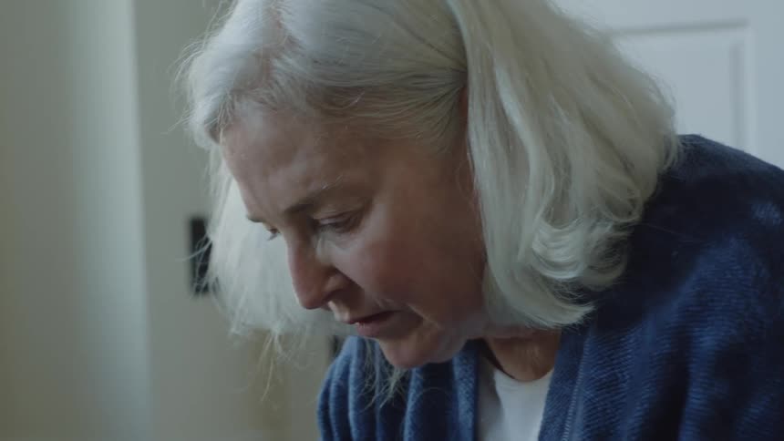 An up close of an elderly woman with white short hair as she looks down thinking