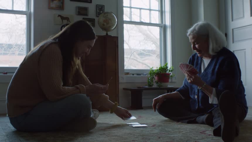 Mother and daughter playing cards over the rug in the living room at home