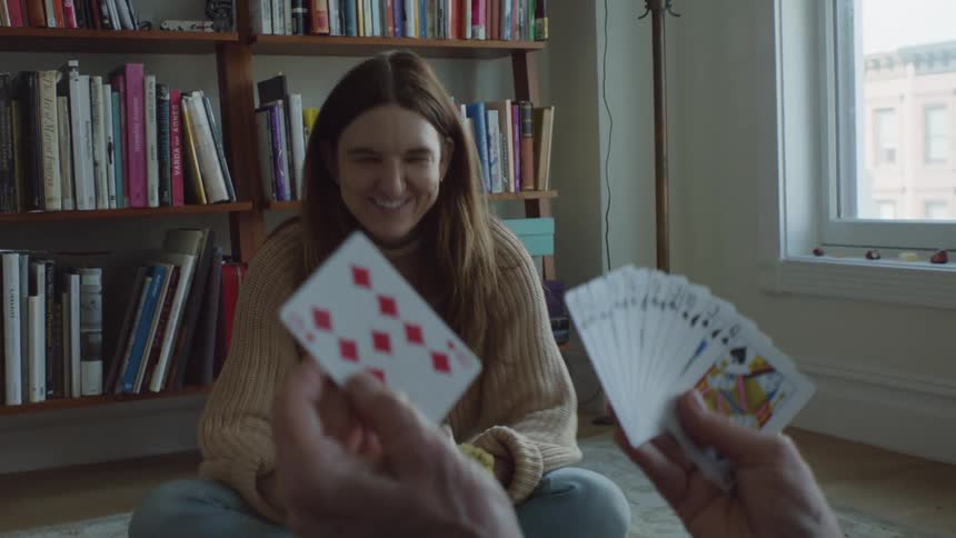 Two women are sitting on the floor playing cards and laughing