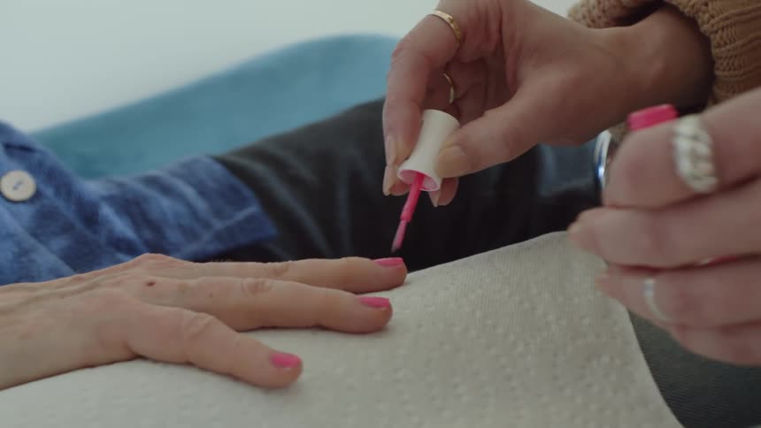 A woman is painting the fingernails of another adult with bright pink nail polish
