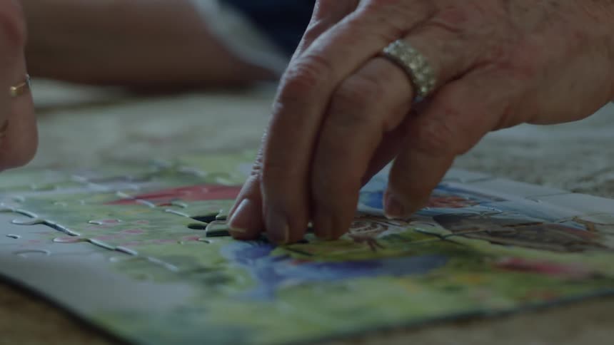 An elderly woman and another woman work together to complete a puzzle