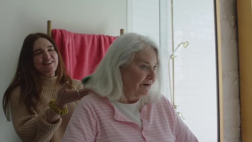 A grandaughter brushes her grandmothers hair in the bathroom as they have a conversation