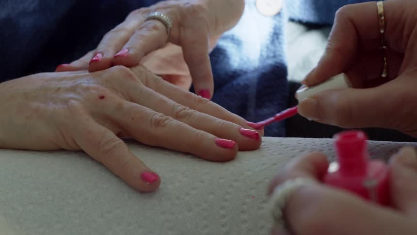 A womans hands are shown having her fingernails painted by another woman whose hands are also the only part shown