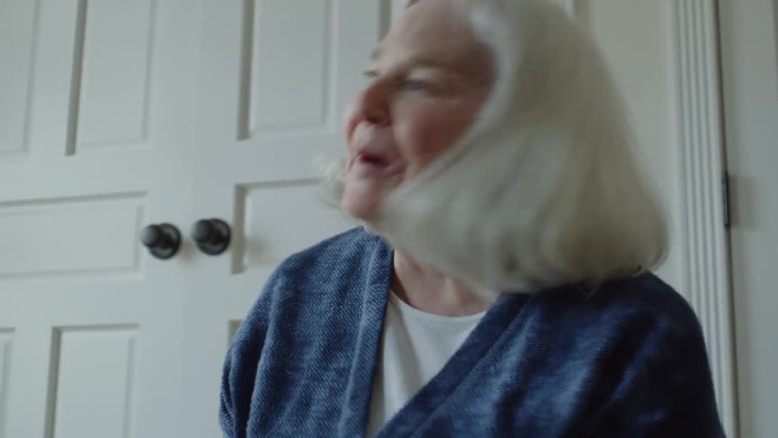 Senior woman with long white hair laughs while playing in the living room floor