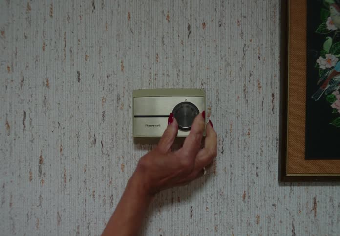 A woman with painted fingernails adjusting a thermostat