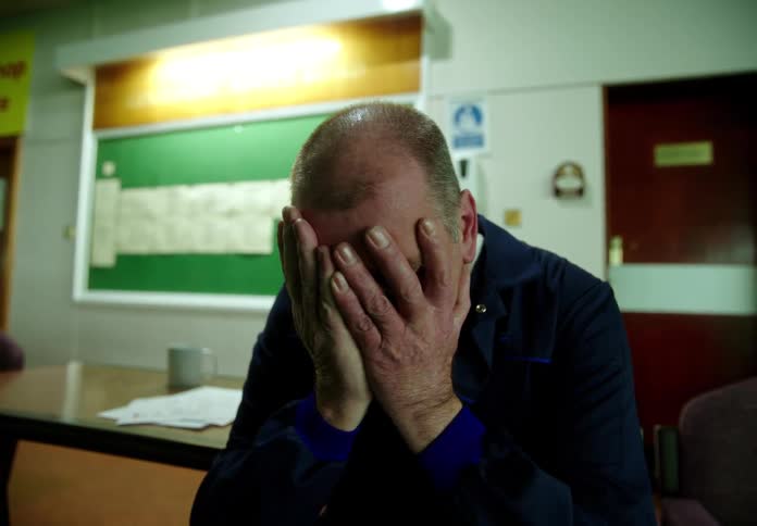Elderly man sitting in waiting area in hospital with face in hands shaking and looking very worried