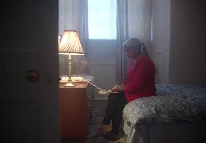 A woman sitting on a bed lowers a phone from her ear while looking sad