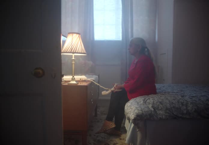 Older woman sits at foot of bed holding phone receiver