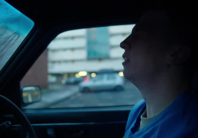 Medical professional wearing face mask and scrubs gets into car and removes mask before crying