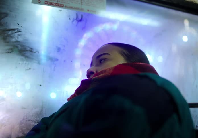 Woman with coat and red scarf travels on empty bus at night in the city