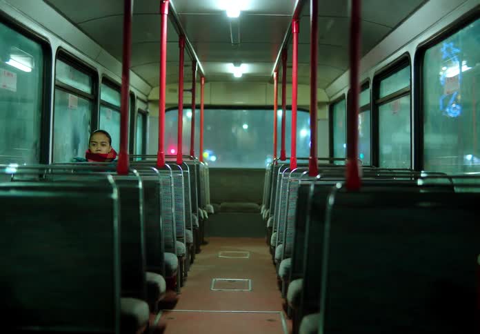 Female passenger sits on empty bus at night as it travels through city