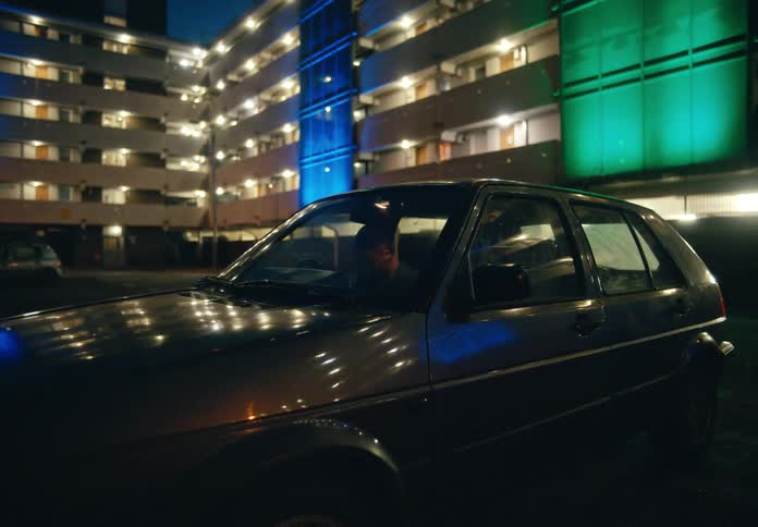Sad male nurse sits inside his car with lights on in the hospital parking lot